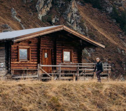 Dieses Bild zeigt eine Hütte und eine Wanderin im Herbst in den Bergen von Gastein