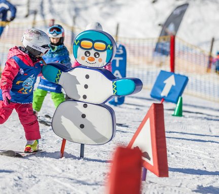 Dieses Bild zeigt ein Kind, dass in einem Snow Park für Kinder fährt und dabei einem Schneemann-Aufsteller ein High-Five gibt