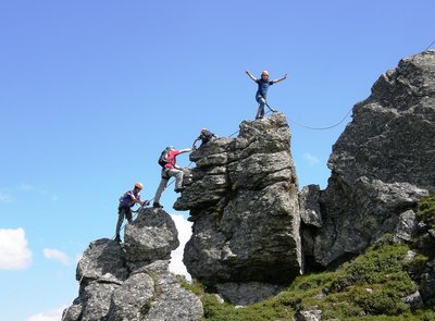 Dieses Bild zeigt eine Gruppe, die auf Felsen des Klettersteiges Hirschinger in luftiger Höhe klettert