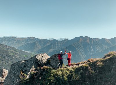 Dieses Bild zeigt zwei Freunde, die einen Klettersteig in Gastein absolvieren und sich dabei ein High-five geben