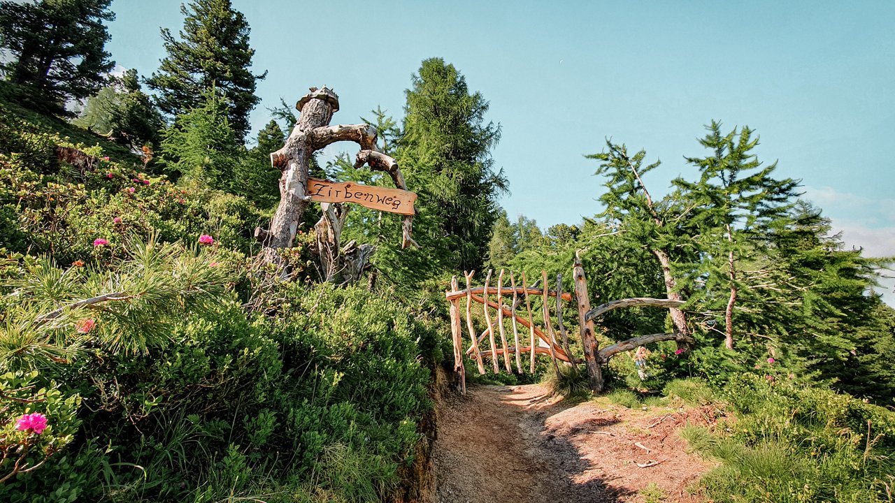 Dieses Bild zeigt ein Tor aus Holz und ein Schild mit der Aufschrift "Zirbenweg"