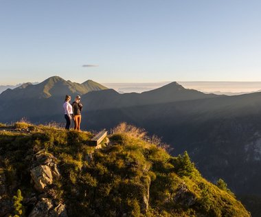 Dieses Bild zeigt zwei Frauen, die auf dem Graukogel stehen und das Bergpanorama bei Abend genießen. 