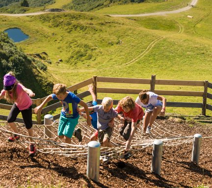 Dieses Bild zeigt eine Familie, die auf der Schlossalm in einem Spielplatz auf ein Kletternetz klettert