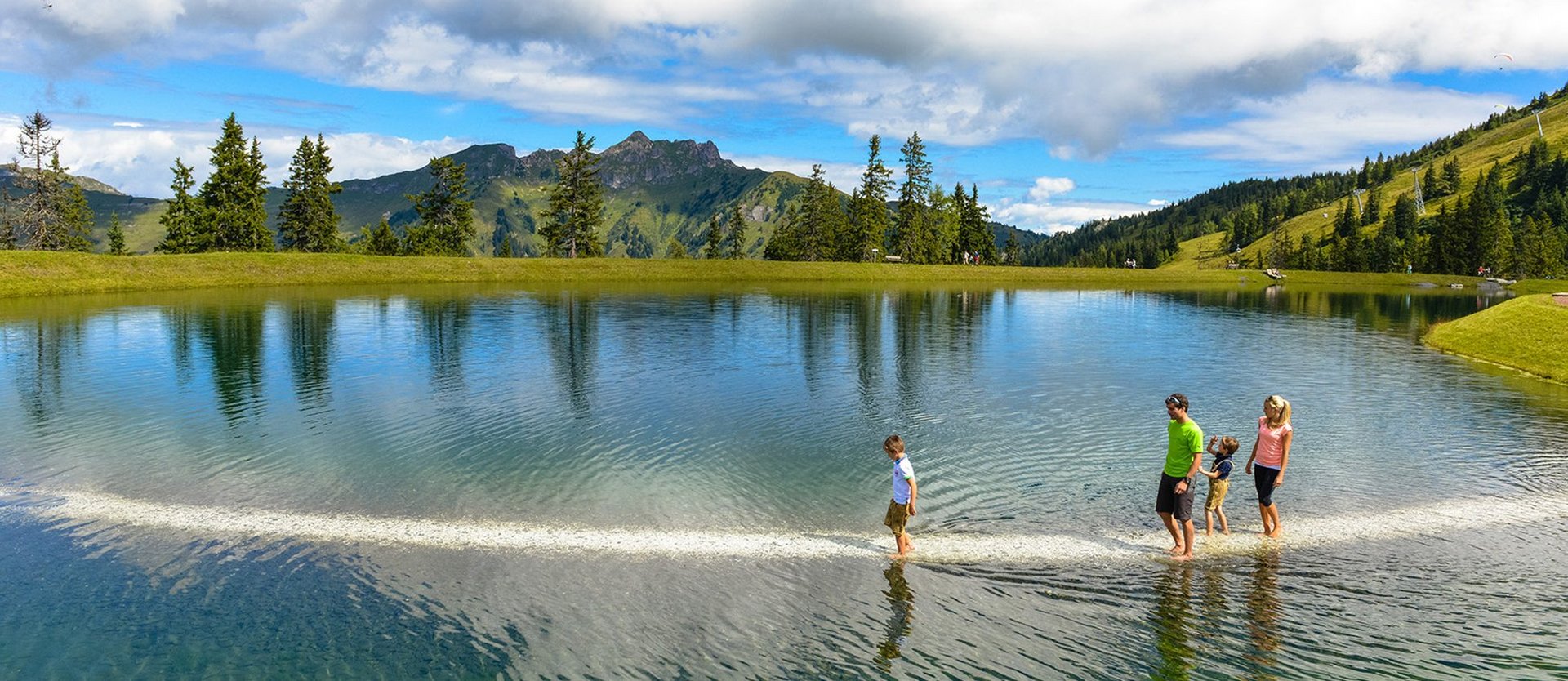 Dieses Bild zeigt eine Familie, die den Barfußweg in Fulsek geht. Dabei geht sie auf einem Weg Barfuß durch den See