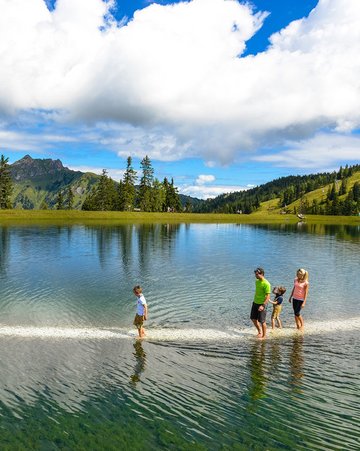 Dieses Bild zeigt eine Familie, die den Barfußweg in Fulsek geht. Dabei geht sie auf einem Weg Barfuß durch den See