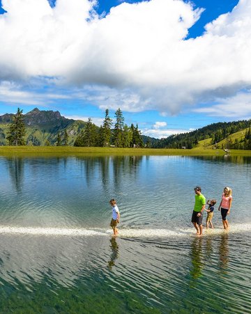 Dieses Bild zeigt eine Familie, die den Barfußweg in Fulsek geht. Dabei geht sie auf einem Weg Barfuß durch den See