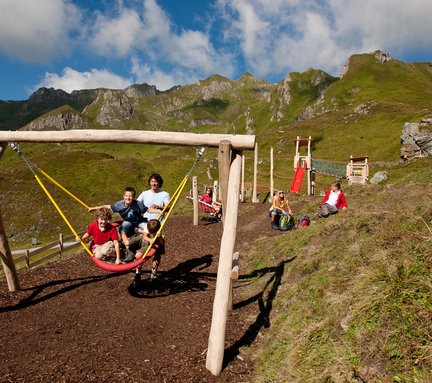Dieses Bild zeigt eine Familie, die auf dem Spielplatz auf der Schlossalm mit einer Nestschaukel schaukeln