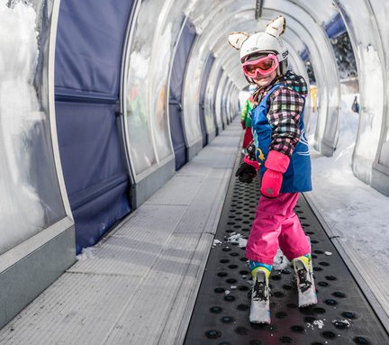 Dieses Bild zeigt ein Skischulkind, dass in einem Förderband nach oben fährt