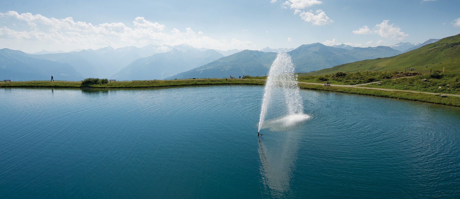Dieses Bild zeigt den Schlossalmsee mit einer Wasserfontäne in der Mitte