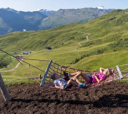 Dieses Bild zeigt zwei Kinder in einer Hängematte in dem Spielplatz auf der Schlossalm