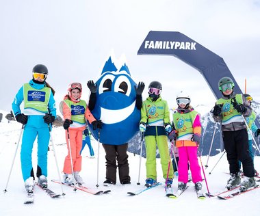 Dieses Bild zeigt eine Gruppe von Skischülern mit dem Maskottchen Gasti vor dem Familypark in Gastein