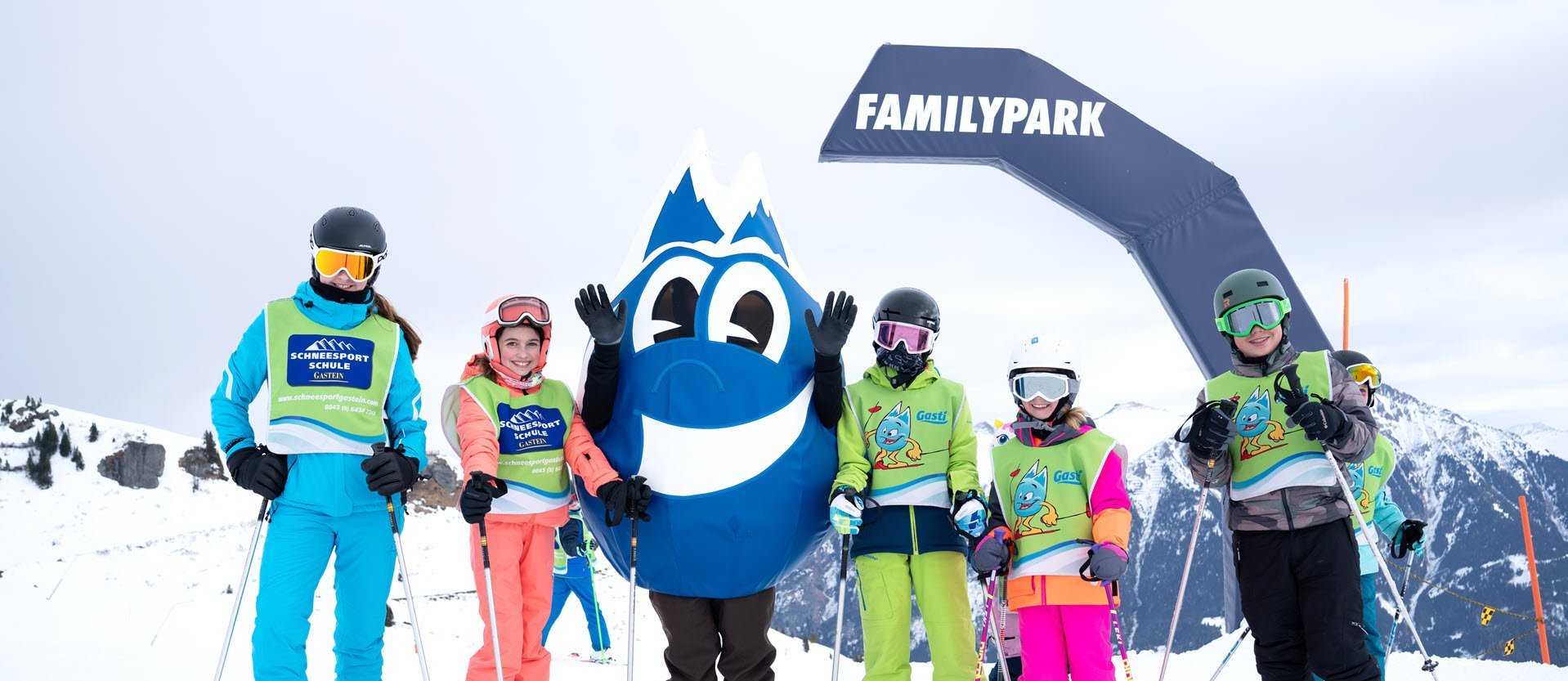 Dieses Bild zeigt eine Gruppe von Skischülern mit dem Maskottchen Gasti vor dem Familypark in Gastein