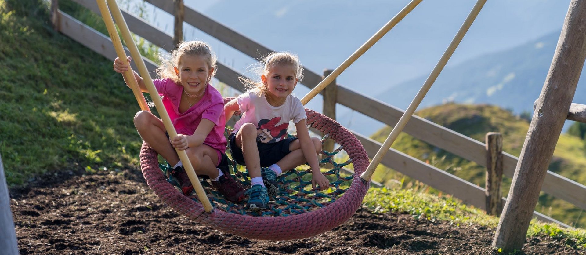 Dieses Bild zeigt zwei Mädchen, die in einer Nestschaukel in einem Gasteiner Spielplatz schaukeln