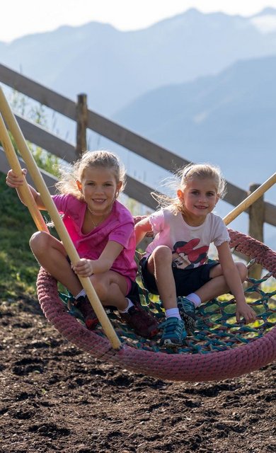 Dieses Bild zeigt zwei Mädchen, die in einer Nestschaukel in einem Gasteiner Spielplatz schaukeln