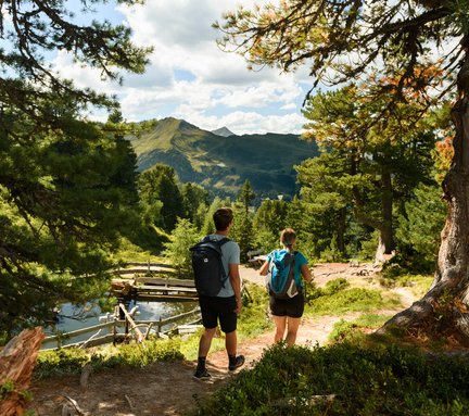 Dieses Bild zeigt ein Paar, das auf dem Graukogel  auf dem Zirbenweg zu einem kleinen See wandert