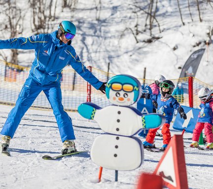 Dieses Bild zeigt einen Skilehrer, der mit Skischulkindern in einen Snowpark für Kinder fährt