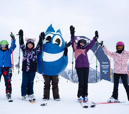 Dieses Bild zeigt eine Gruppe von Kindern mit Ski mit dem Maskottchen Gasti vor dem Familypark in Gastein